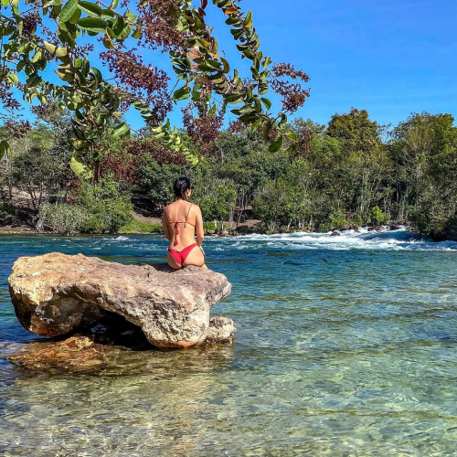 Foto de uma mulher sentada em uma pedra, de costas, em um rio.